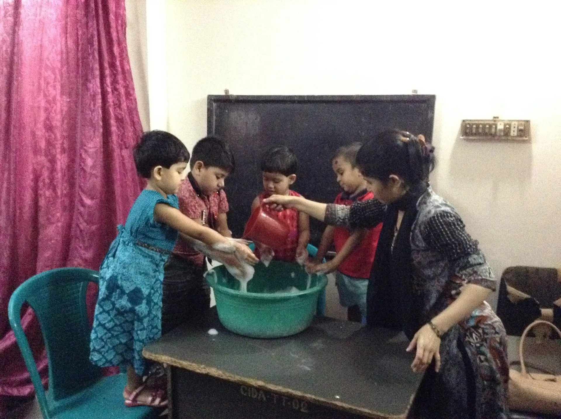 A teacher helps young children wash their hands in a basin in a classroom