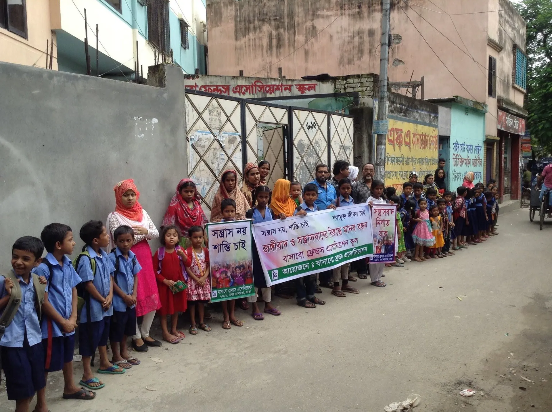 Students in school uniform, guardians and teachers stand in a line along a Bashabo street, holding banners against terrorism and extremism