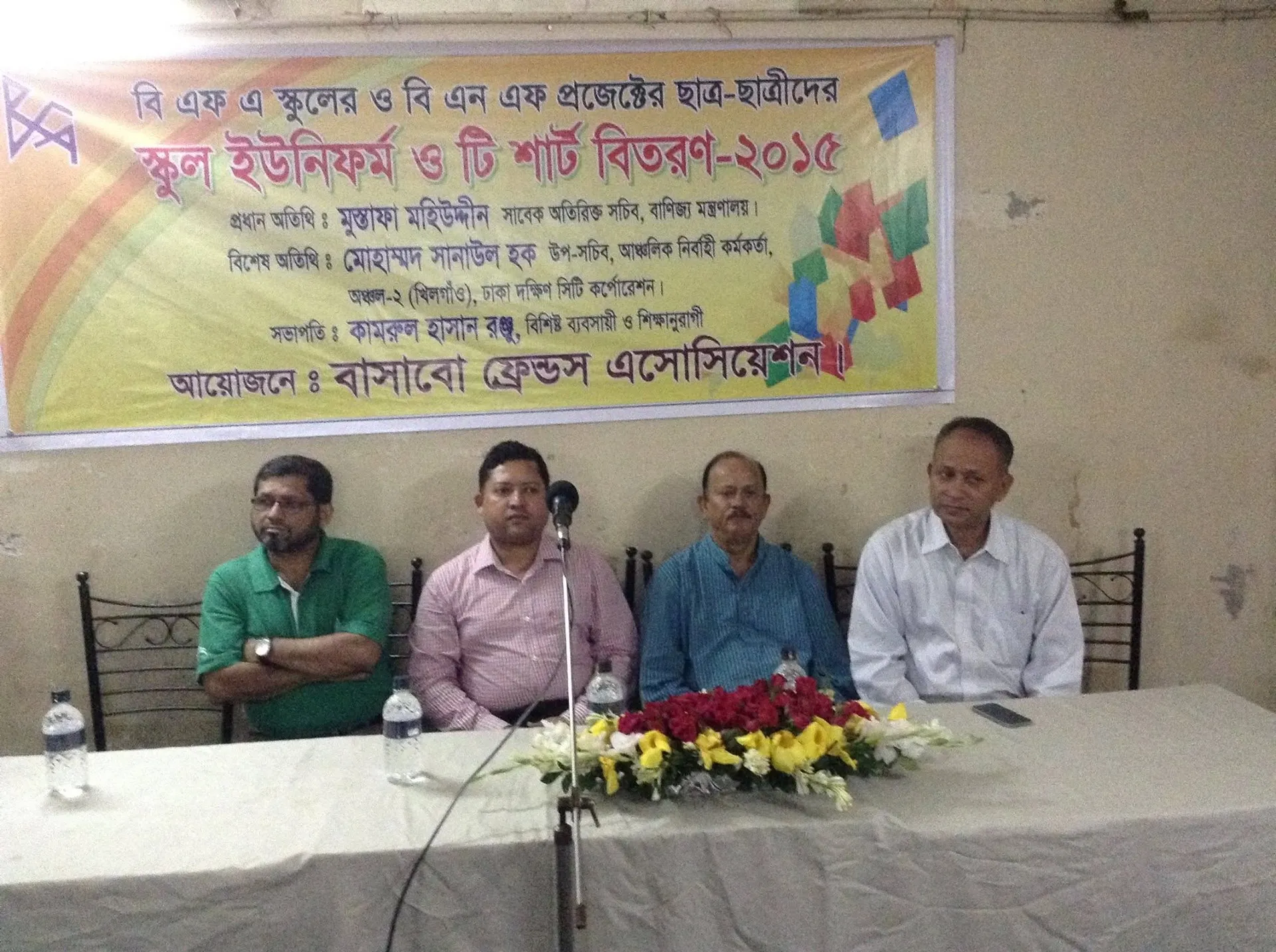 Guests seated at a table under a banner for the 2015 school uniform and T-shirt distribution